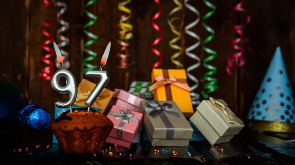 Birthday background with muffin and candles with number  97. Beautiful anniversary background with cake copy space with burning candles. Gift boxes with decorations.