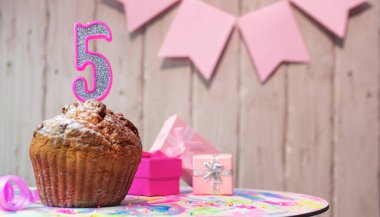 Festive cake or muffin with a pink candle with a number  5. Happy birthday background with a number for a girl or woman with beautiful decorations. Anniversary party copy space.