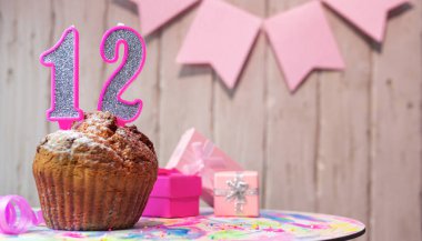 Festive cake or muffin with a pink candle with a number  12. Happy birthday background with a number for a girl or woman with beautiful decorations. Anniversary party copy space.