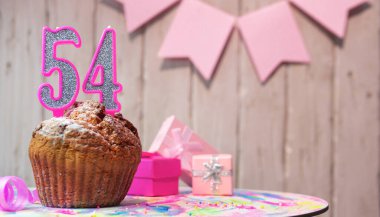 Festive cake or muffin with a pink candle with a number  54. Happy birthday background with a number for a girl or woman with beautiful decorations. Anniversary party copy space.