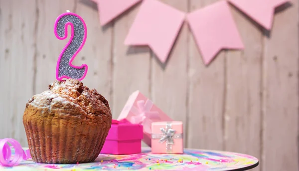 Festive cake or muffin with a pink candle with a number  2. Happy birthday background with a number for a girl or woman with beautiful decorations. Anniversary party copy space.