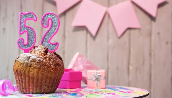 Festive cake or muffin with a pink candle with a number  52. Happy birthday background with a number for a girl or woman with beautiful decorations. Anniversary party copy space.