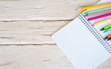 Üzerinde siyah tuşlu kalem olan bir kafesin içinde boş bir sayfa olan üst görünüm not defteri. Ahşap bir masanın üzerinde renkli kalemlerle yazılmış bir yazı için boş. Yazmak için boş form