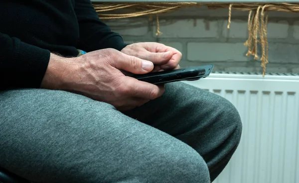 Elderly man with a smartphone in his hands. Grandpa holds a smartphone in his hand. Flipping a finger on the screen screen on a smartphone. Online order on the Internet.