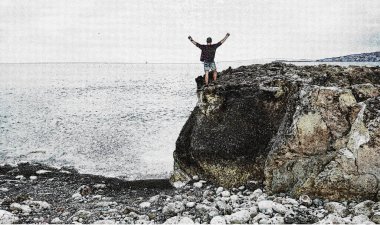 Happy man on top of a mountain with his hands up in the background of the sea. Dreamy man on the mountain. The man looks at the sea.
