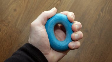Rubber carpal expander blue in a person's hand. Doing sports at home. Lifestyle. Rehabilitation Restoration of the hand after an injury. A man pumps up his arm with an exercise.