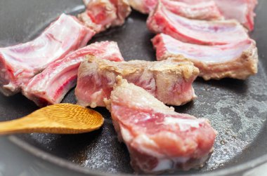 Fry rib meat in a pan. Stir the meat with a wooden spoon. Close-up of juicy meat meat cooking in the kitchen.