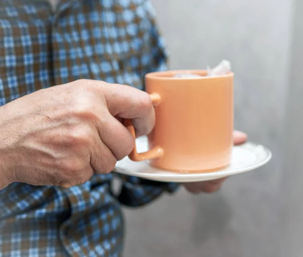 Hands of an elderly man with a mug of tea. A man holding a cup of hot fragrant medicinal tea.