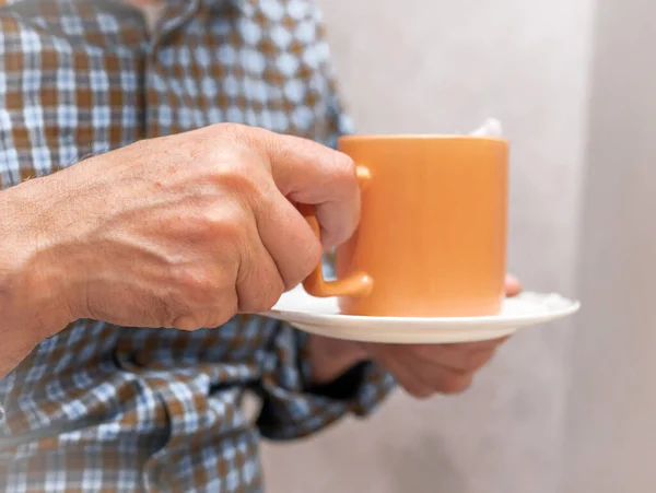 Hands of an elderly man with a mug of tea. A man in a plaid shirt holding a cup of hot fragrant medicinal tea.