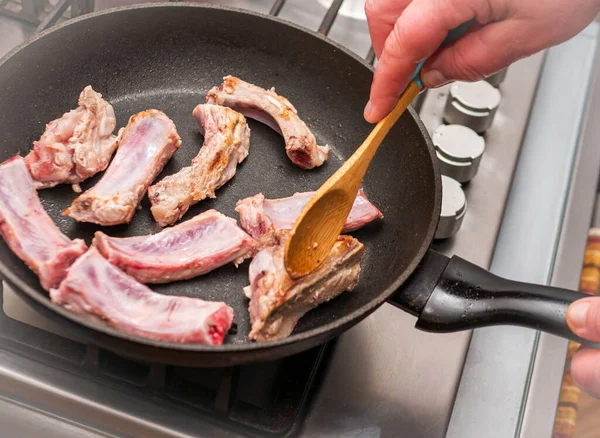 Woman Fry rib meat in a frying pan. Stir the meat with a wooden spoon. Close-up of juicy meat meat cooking in the kitchen.