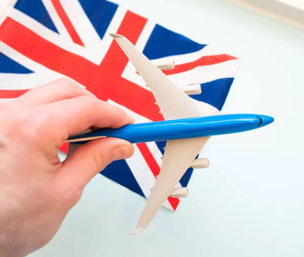 Top view Passenger blue plane flying over UK flag. The concept of tourism and travel around the world. A flying plane in a man\'s hand.