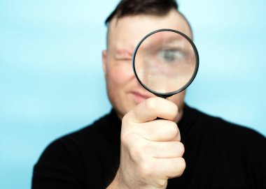 The concept of healthy vision in people. Young man Looking through the glass is fascinating. A young guy with a magnifying glass magnifying his eye. Positive cheerful creative photo with a man