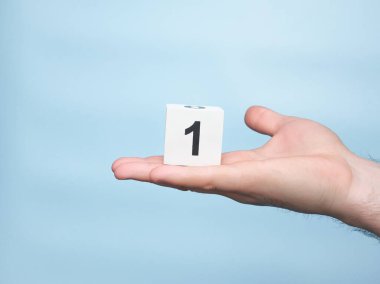 Young man's hand holding cube with number 1 on blue copy space background