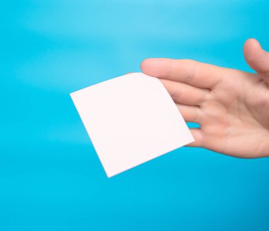 A hand holds a blank letter sticker for your text inscription. Message on sticker copy space. Mini banner for text in a person's hand. On a light pastel background