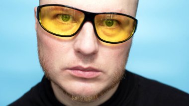 Portrait of a handsome young man in yellow anti-fare sunglasses, on a blue background. A man in glasses for cycling.
