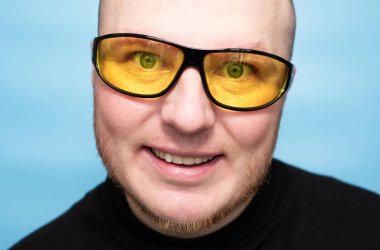 Portrait of a handsome man with a smile A young man in yellow anti-fare sun glasses, on a blue background. A man in glasses for cycling.