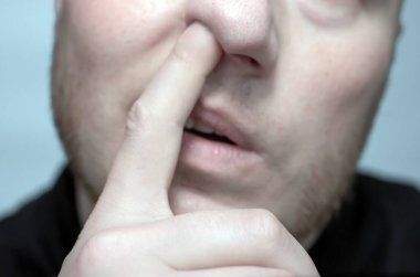 The man picks his nose. Close-up of a man with a finger in his nose.