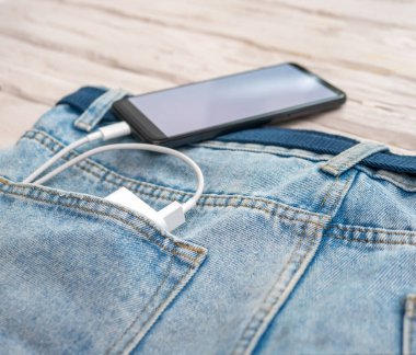 USB cable with smartphone charger in jeans pocket. Smartphone with white screen copy space. Charging phone with usb cable