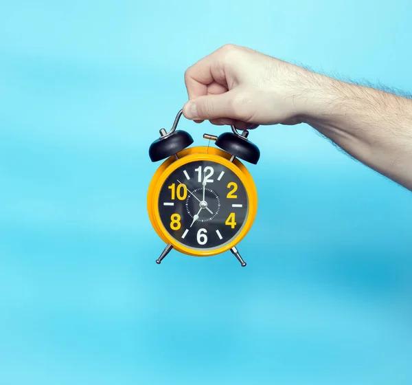 Clock time concept. Alarm clock in a man\'s hand on a blue background on the clock hands 7 in the morning. Studio shot with a retro clock with an alarm clock.
