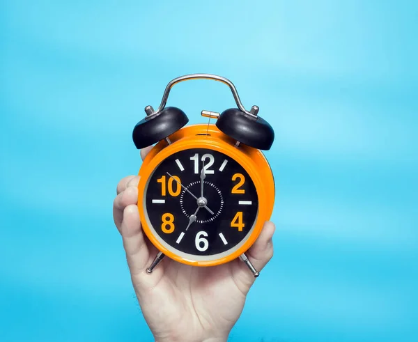 Clock time concept. Alarm clock in a man\'s hand on a blue background on the clock hands 7 in the morning. Studio shot with retro clock with alarm clock orange
