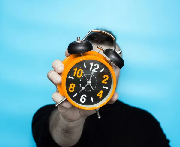 Clock time concept. Alarm clock in a man\'s hand on a blue background on the clock hands 7 in the morning. Studio shot with young man with retro clock with alarm clock orange
