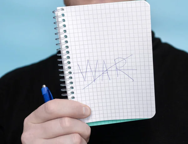 Notepad in a man\'s hand with the inscription war. The word war is crossed out with a pen on paper. No war banner