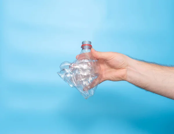 The concept of plastic garbage, care for the environment. Twisted squeezed used plastic white bottle in the hand of a young man on a blue background. Space copy.