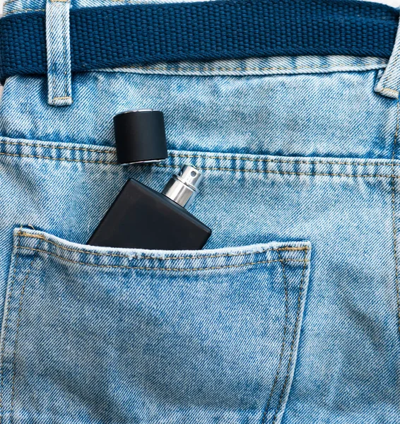 Top view of a black jar with men\'s perfume without a logo in a jeans pocket. Perfume for men in the pocket of men\'s pants.