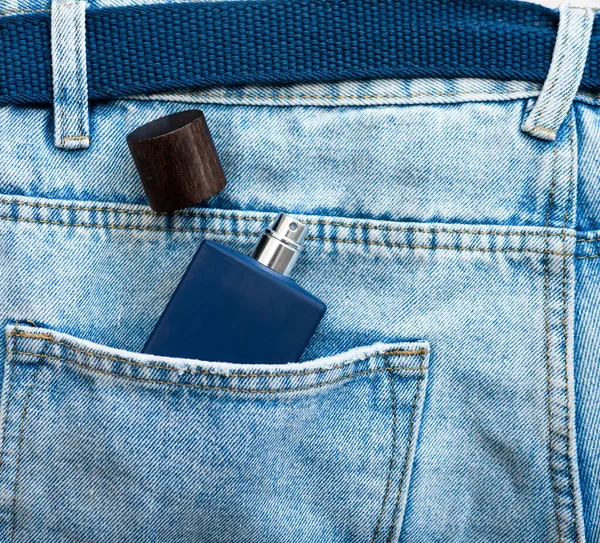 Top view of a blue jar with men\'s perfume without a logo in a jeans pocket. Perfume for men in the pocket of men\'s pants.
