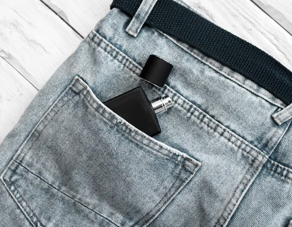 Top view of a black jar with men's perfume without a logo in a jeans pocket. Perfume for men in the pocket of men's pants. black and white
