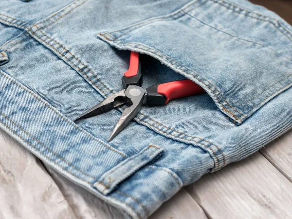 Pliers with a red handle in the pocket of jeans pants. The concept of repair and construction, construction tools in the pocket of the chaton.