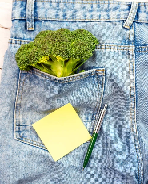 Top view bunch of broccoli with notepad or sticker blank for text in denim pocket. Green tree on denim. Notes for inscription