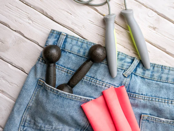 The concept of manufacturing sports goods and accessories for sports. Dumbbells in the pocket of jeans or shatans. Rope with an elastic band for sports.