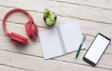 Top view Over-ear red headphones with a smartphone with a white display. Headphones with notepad and writing pen. Desktop. Online education. Home Office. copy space