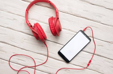 Top view Overhead red headphones with smartphone with white screen for text. Desktop. Online education. Home Office. copy space