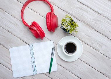 A cup of black coffee, overhead Musical headphones with a notepad with a blank page for text. Work desk with smartphone notepad and pen. Copy space. Office desk top view.