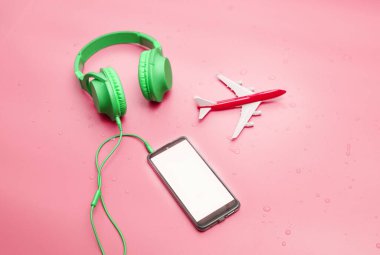 Top view Green overhead music headphones in water drops, with travel airplane, copy space. Headphones on a pink pastel background on a wet surface. Place for text. Background mp3.