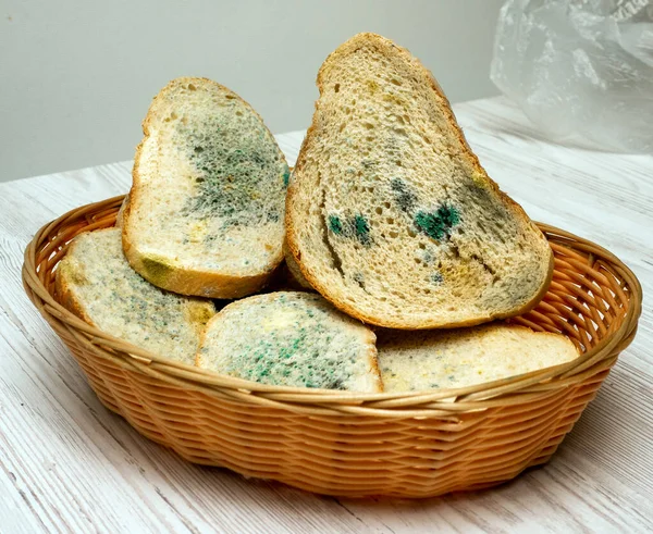 Bread with mold in a straw basket on a light wooden table in the kitchen, bread with fungus, food poisoning, microbes. Flowered bread.