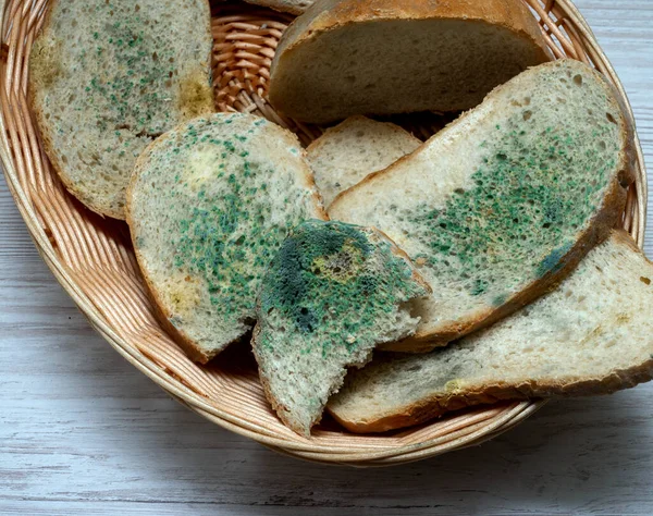 Top view, Bread with mold in a basket of straw on a light wooden table in the kitchen, harmful bread with fungus, harmful food contamination, microbes. Flowered bread.