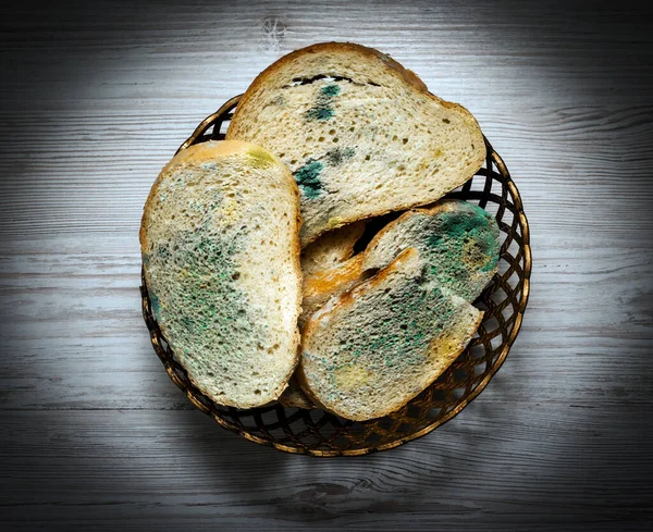 Top view, Bread with mold in a grocery basket, on a light wooden table in the kitchen, harmful bread with fungus, harmful food contamination, microbes. Flowered bread.