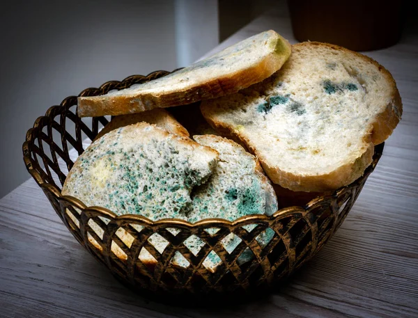 Close-up, Bread with mold in a grocery basket, on a light wooden table in the kitchen, harmful bread with fungus, harmful food contamination, microbes. Flowered bread.