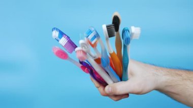  Different toothbrushes in a man's hand on a blue background. A set of multi-colored toothbrushes in a male hand. Oral hygiene concept. Care for bugs