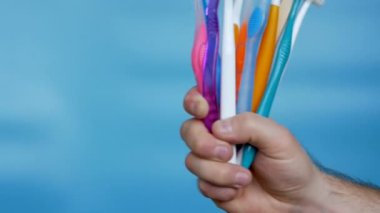 Different toothbrushes in a man's hand on a blue background. A set of multi-colored toothbrushes in a male hand. Oral hygiene concept. Care of human obsessions.