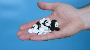Mavi arka planda bir adamın elindeki tıbbi haplar. Hapları yavaş çekim kamerasına dök. Sağlık konsepti. Bir adamın elindeki antibiyotik kapsülleri.
