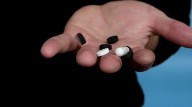 Medical pills capsules in a man's hand, pouring pills into his hand. Pour capsules into your hand. On a blue background, In slow motion. Medicine concept. Treatment with tablets