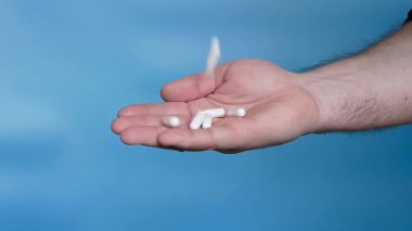 Medical pills capsules are white in a person's hand on a blue background in slow motion, pouring pills into a hand. Medicine concept. Treatment with tablets