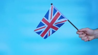 The flag of England in the hand of a man on a blue background, Britain's flag. The flag of the United Kingdom of Great Britain develops in the wind.