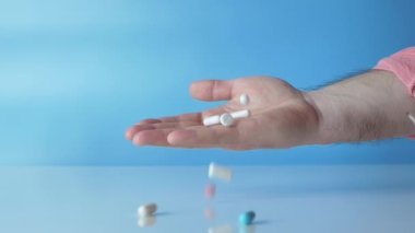 Human health concept. Falling pills in a person's hand in slow motion on a blue background. Medical capsules, antistress tablets. Pharmaceutics. Antibiotic tablets.