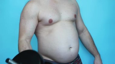 Obesity belly in a man is a big inflated, fat young man with a big belly with a dumbbell in his hand, pumping biceps with a belly. Skin sagging from obesity. The concept of losing weight by training in the gym.