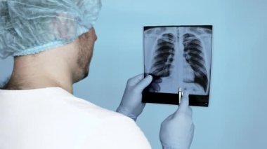 Steril eldivenli, doktor cüppeli ve kepli bir doktor. Ameliyathanede ellerinde akciğerlerinin röntgeni var. Bir doktor hastanede birinin akciğerlerinin röntgenini dikkatlice analiz eder..